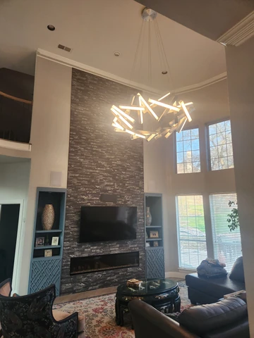 Two-story living room remodel in Garland, TX with a stone fireplace and chandelier