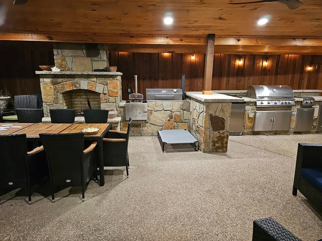 Covered outdoor kitchen in Garland, TX with a stone fireplace and built-in grills