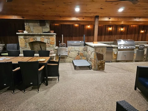 Covered outdoor kitchen in Garland, TX with a stone fireplace and built-in grills